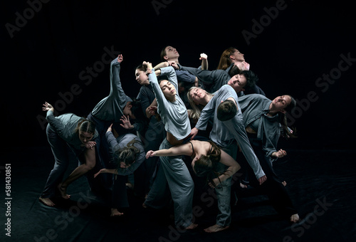 Group of young people in gray stage costumes making performance  dancing against black studio background. Concept of modern freestyle dance  contemporary art  movements  hobby and creative lifestyle