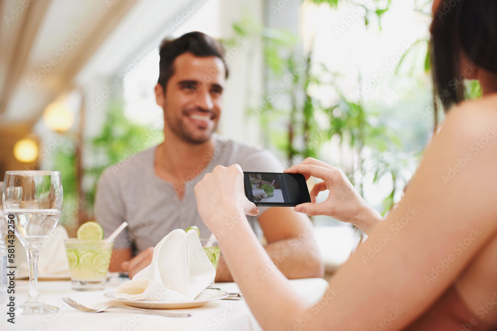 One for her cocktail album. A woman taking a picture while dining out with her partner at a restaurant. One for her cocktail album. A woman taking a picture while dining out with her partner at a restaurant.