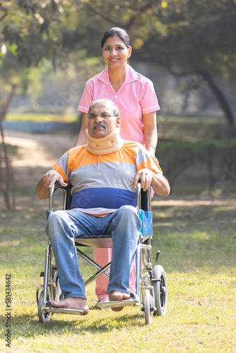 Nurse talking to male senior patient on wheelchair with a neck brace at the park.
