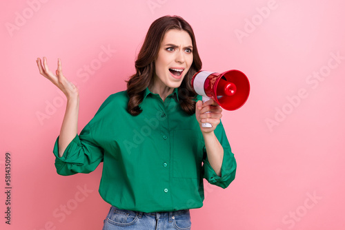 Photo of angry bossy woman wavy hairdo dressed green shirt shouting in loudspeaker blaming look empty space isolated on pink background