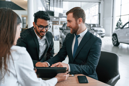 Two men are buying automobile. Three people are working together in the car showroom