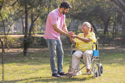 Male physical therapist discussing with senior woman in wheelchair at park. © G-images