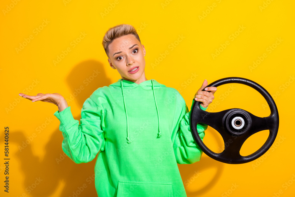 Portrait of clueless girl hand hold wheel shrug shoulders isolated on yellow color background - obrazy, fototapety, plakaty 