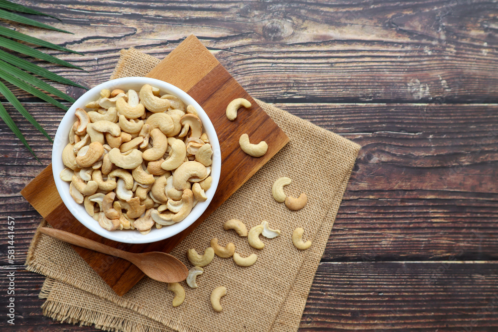 Fototapeta premium Cashew nuts in white bowl on wood table - Top view with copy space