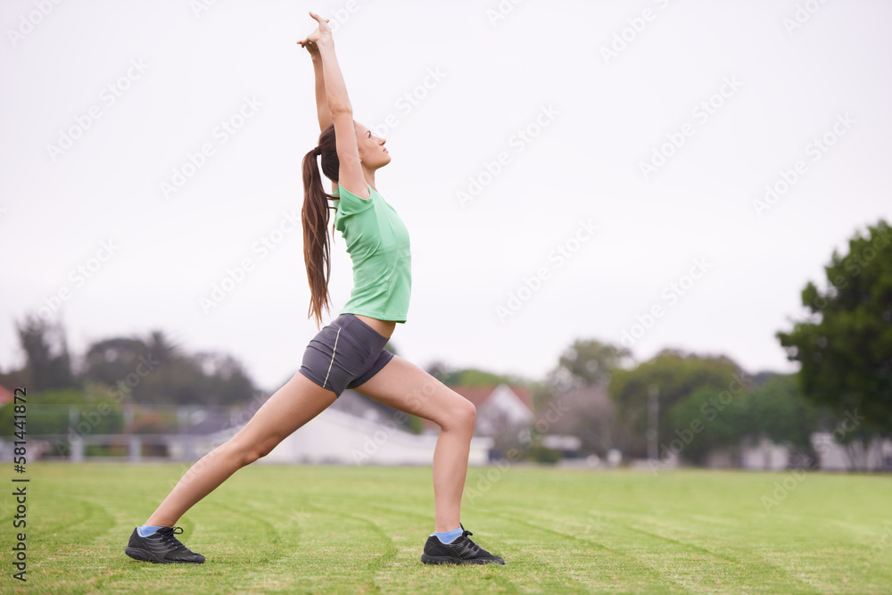 Focus on the burn. a young woman stretching on a grassy field.