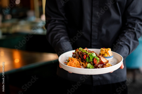 chef hand hold plate whith Stewed pork slice with noodles and vegetables