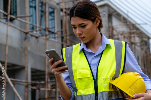 Female engineer in safety gear wearing hard hat using mobile phone at construction site