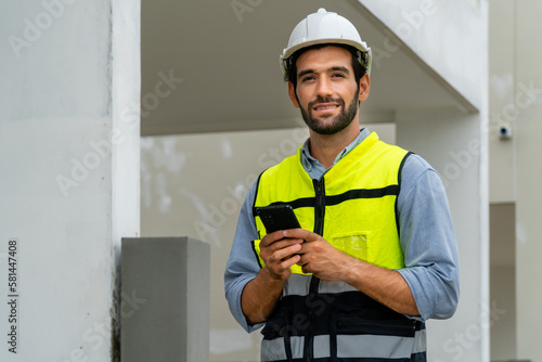 engineer in safety gear wearing hard hat using mobile phone at construction site