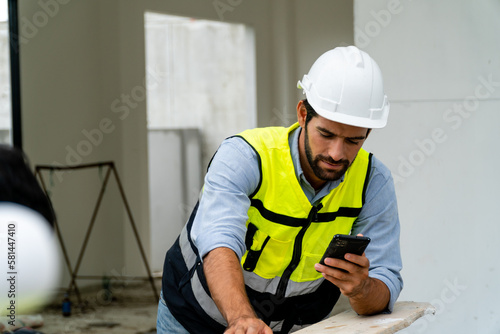  engineer in safety gear wearing hard hat using mobile phone at construction site
