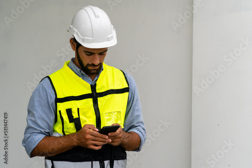  engineer in safety gear wearing hard hat using mobile phone at construction site