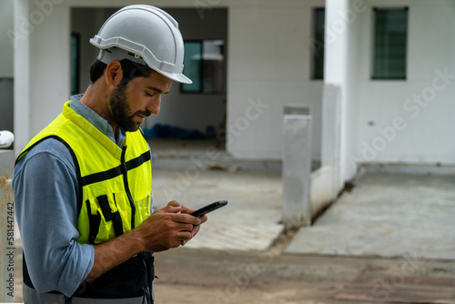  engineer in safety gear wearing hard hat using mobile phone at construction site