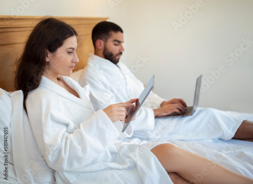 Freelancers Spouses Using Digital Tablet And Laptop Computers In Bedroom