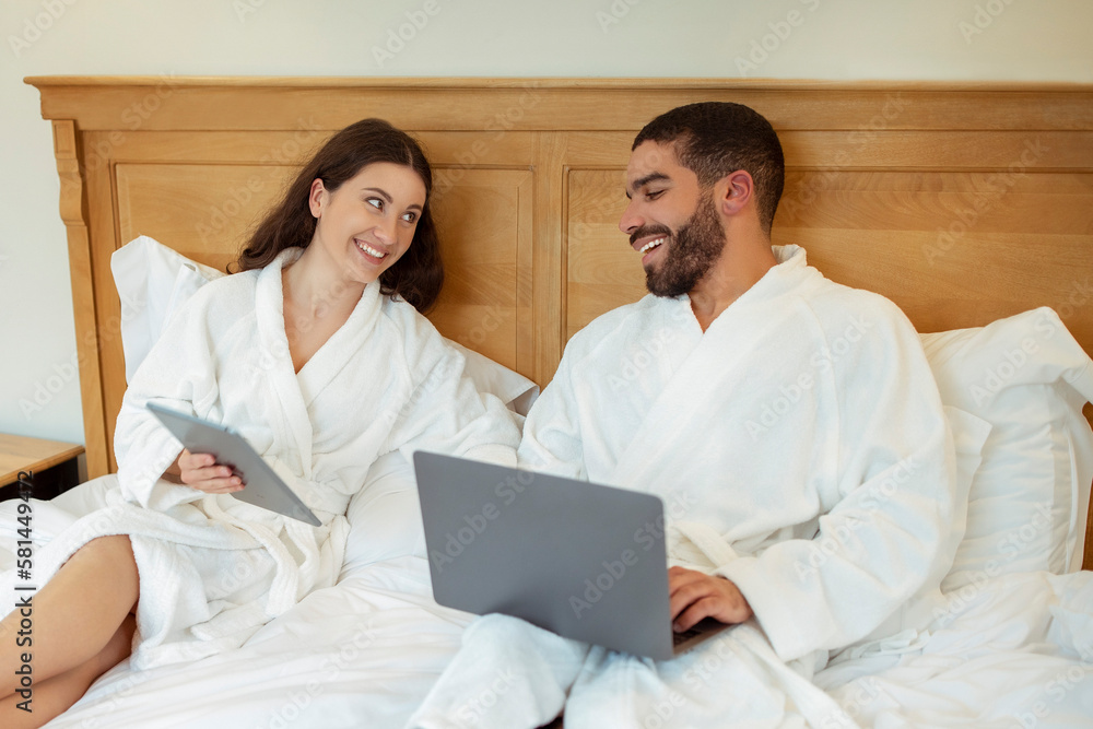 Husband And Wife Browsing Internet On Computers Sitting In Bedroom Husband And Wife Browsing Internet On Computers Sitting In Bedroom