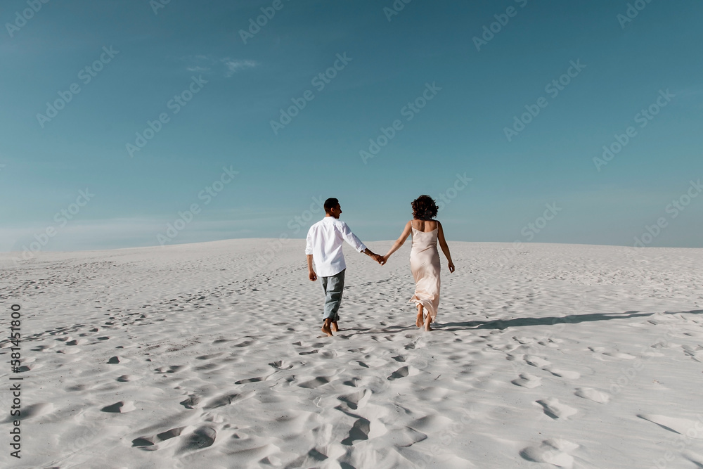 Young couple enjoying while walking in dunes. Romantic traveler walking through the Sahara desert. Adventure travel lifestyle concept. (selective focus)