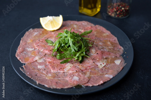 Marbled beef carpaccio with arugula, parmesan cheese, olive oil and lemon. A traditional classic appetizer made from thinly sliced raw meat. Close-up, selective focus, black background.
