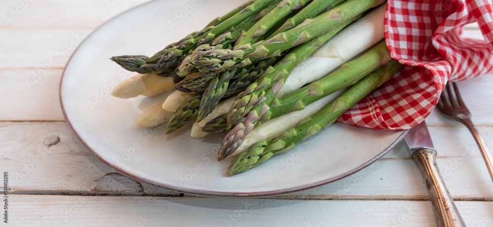 Fresh asparagus on bright ceramic plate. Seasonal vegetables for a healthy nutrion. Background for a gastronomy concept. Close-up.
