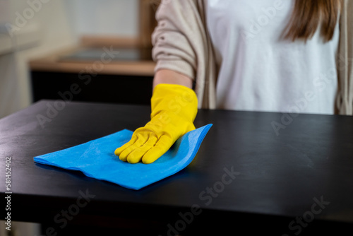 Cleaning service worker cleans the kitchen table at home. Beautiful young female housekeeper wipes dirty table. 