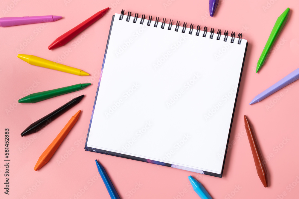 Back to school concept. Colorful wax crayons and white album on pastel pink. Copy space. Top view. Back to school concept. Colorful wax crayons and white album on pastel pink. Copy space. Top view.