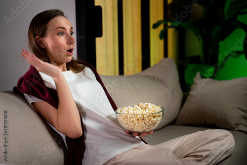 Shocked woman watches a horror movie with popcorn sitting on the sofa in the living room. 