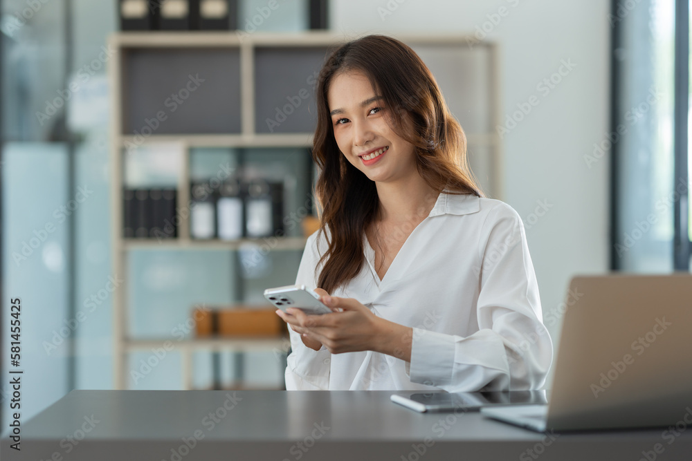 Beautiful Asian businesswoman working on a laptop computer using a mobile phone to negotiate financial business accounting analysis, report, and office information. Beautiful Asian businesswoman working on a laptop computer using a mobile phone to negotiate financial business accounting analysis, report, and office information.