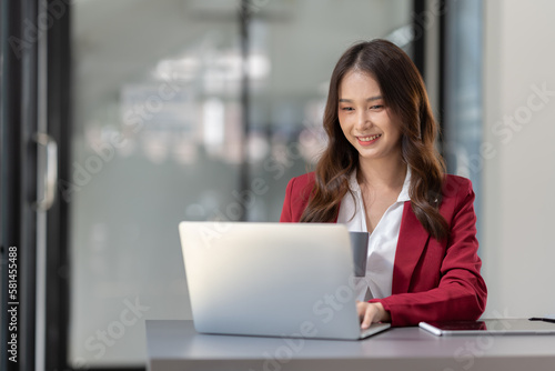 Beautiful Asian businesswoman holding a cup of coffee relax Take breaks and work hard on financial business matters at the office and have fun. Smiling happy working with the laptop.