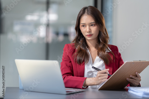 Asian businesswoman sitting in an office looking with graph detail on laptop computer Chart of real estate business growth data in the office. © crizzystudio