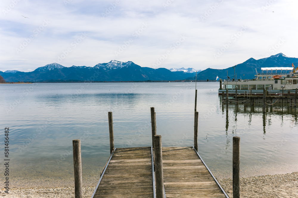 View of the Alps.Alpine lake.Lake near the mountains.Snow in the mountains.Wooden pier.Pier at the lake.Travel agency.Holidays in Germany.Popular tourist destination in Germany.Ship at the pier.Lake.