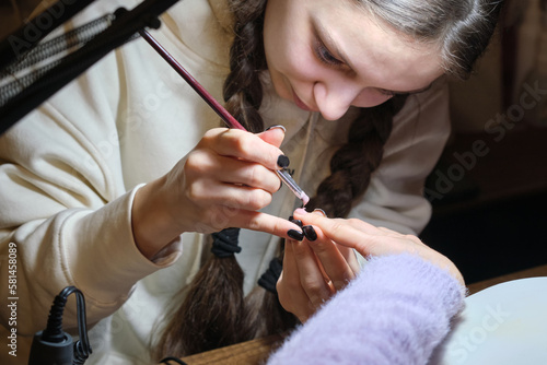 Young female manicurist doing nail extensions to a client in a salon.