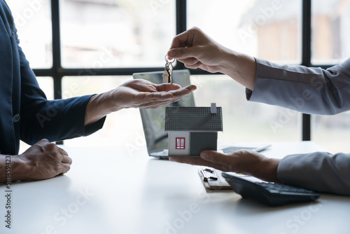 Asian young businessman, architect, engineer handing over house keys on desk in office after agreeing on purchase contract. Or rent to sign a business agreement.