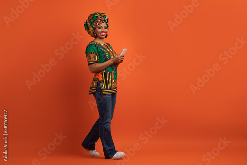 Cool pretty young black woman using smartphone and walking © Prostock-studio