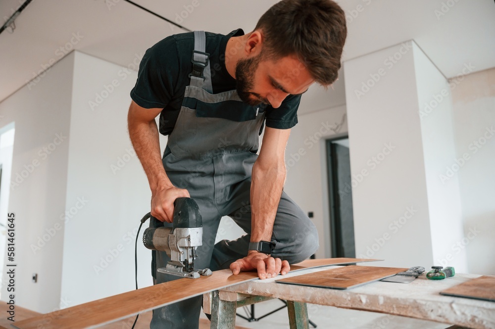 On the table. Cutting planks by the drill. Man is installing new laminated wooden floor On the table. Cutting planks by the drill. Man is installing new laminated wooden floor
