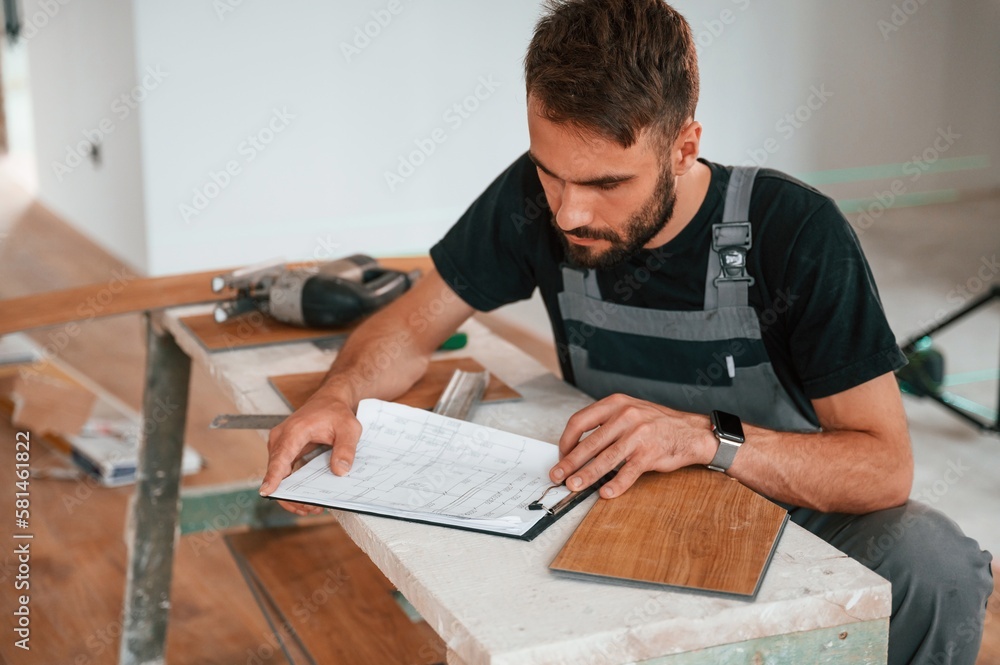 Man sitting by the table and writing data into notebook. With new laminated wooden floor