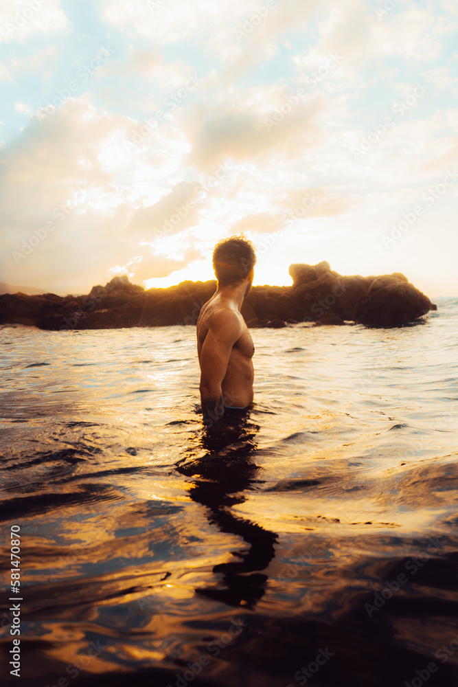 Shirtless man standing in sea against sunset sky