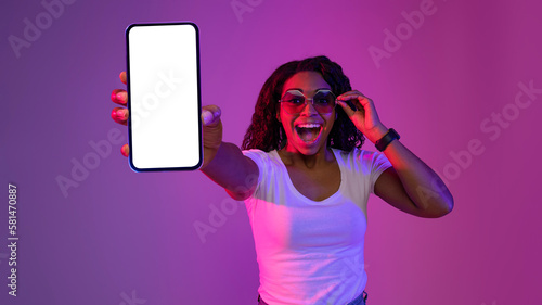 Mobile Mockup. Excited Black Woman In Stylish Sunglasses Demonstrating Blank Smartphone