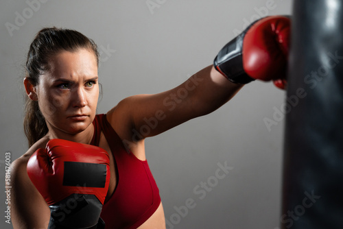 A boxer woman in a red tracksuit hits a punching bag © makedonski2015