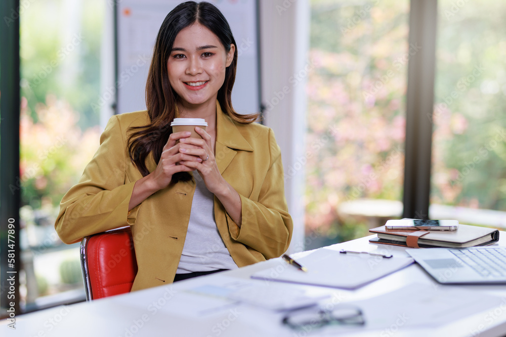 Obraz premium Concept of business office woman working,Businesswoman smile while working about her invesment plan with analyzing document and business investment graph data and holding coffee cup in workstation
