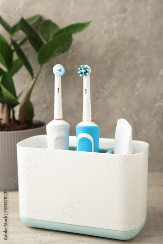 Holder with modern electric toothbrushes and plant on blue background