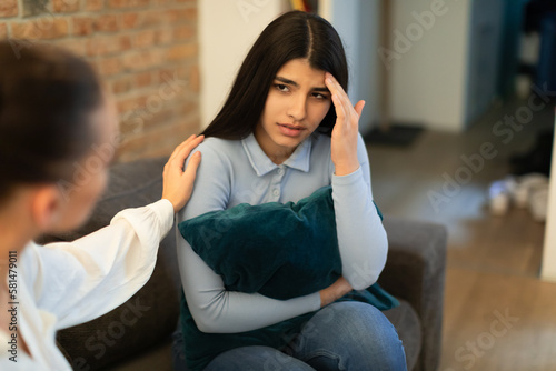 Unhappy teen lady having problem, hugging pillow and talking with friend who showing compassion and trying to appease