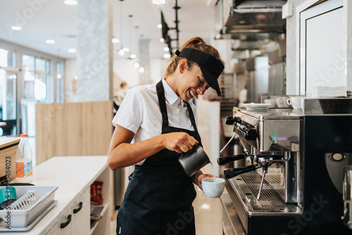 Print op canvas Beautiful and happy young female worker working in a bakery or fast food restaurant and using coffee machine