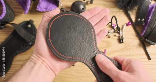 Male hands will check bdsm spanking paddle for erotic games. POV view, a bunch of toys from the sex shop are on the table.