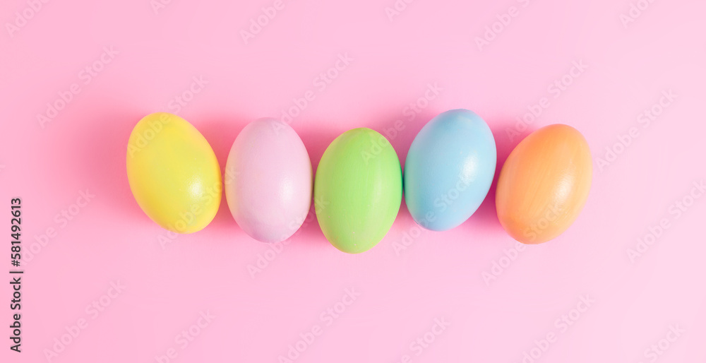 Happy Easter holiday greeting card concept. Colorful Easter Eggs on pastel pink background. Flat lay, top view, copy space.