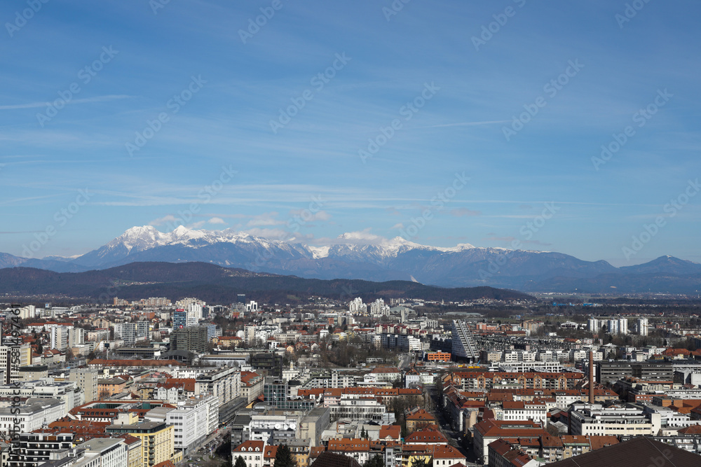 Panoramic city view of Ljubljana, Slovenia with snow on top of mountains on sunny day.