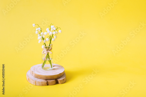 Lilies of the valley bouquet in a miniature jar on a yellow background with copy space