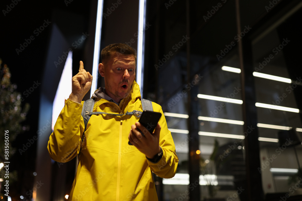 Inspired man with surprised face showing index finger up gesture while looking at his mobile phone. Inspired man with surprised face showing index finger up gesture while looking at his mobile phone.