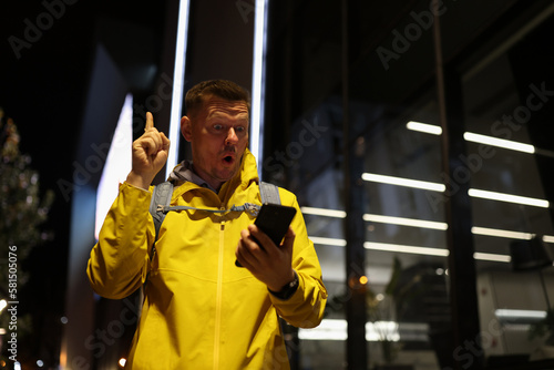 Inspired man with surprised face showing index finger up gesture while looking at his mobile phone.