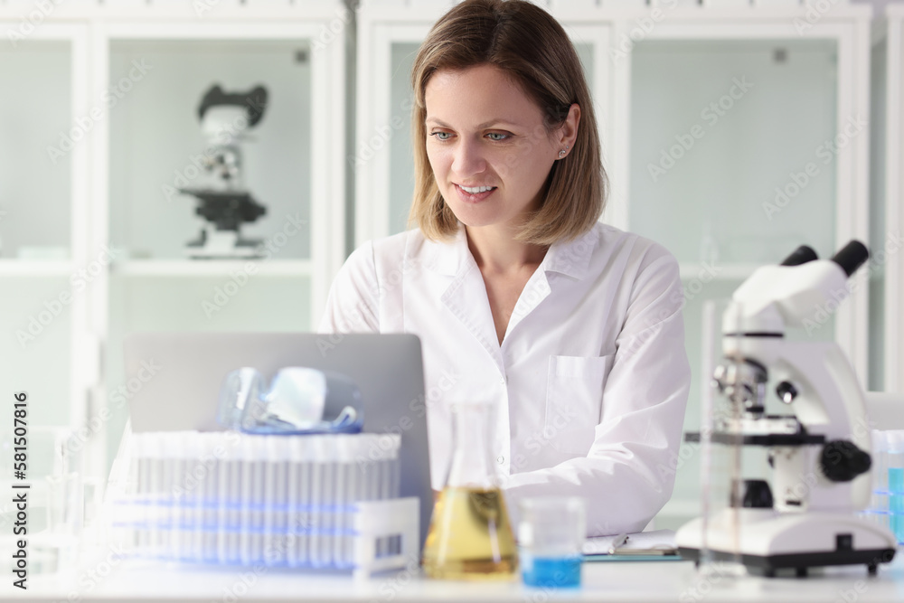 Satisfied female researcher working on laptop at laboratory table. Satisfied female researcher working on laptop at laboratory table.
