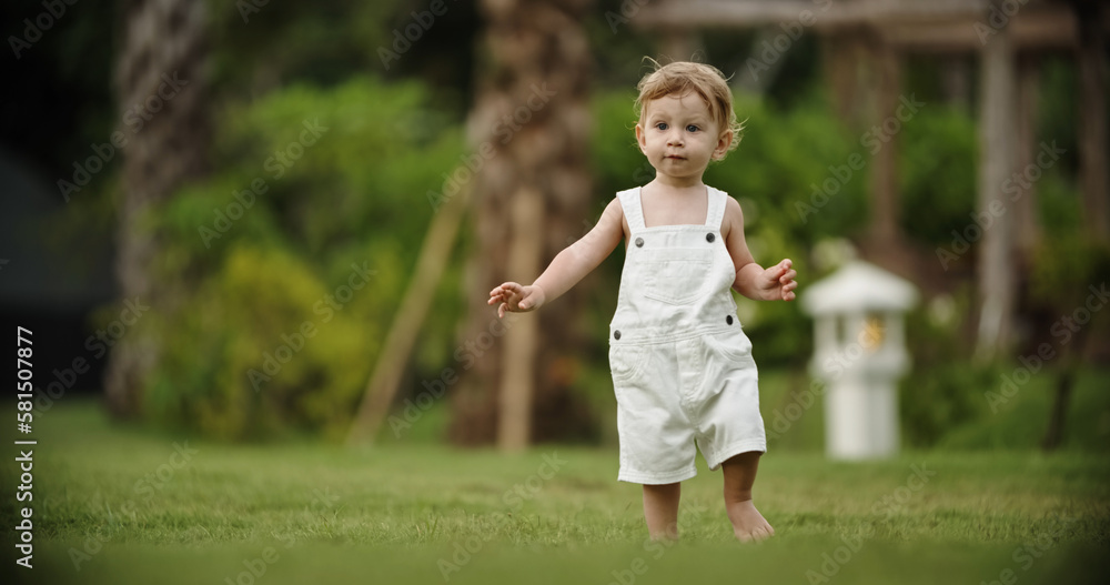 Naklejka premium Little kid in white bodysuit, barefoot. He is smiling, running on grass in the park. Concept for articles about childhood or advertising for babies. Close up. Copy space