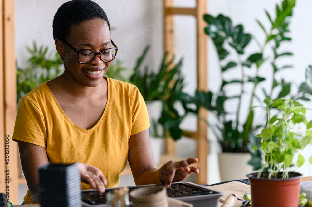 Young smiling african-american woman doing seed-starting early in the spring indoors for her backyard garden or a homestead garden Young smiling african-american woman doing seed-starting early in the spring indoors for her backyard garden or a homestead garden