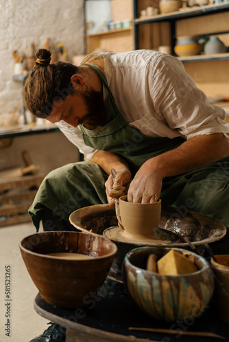 A potter sculpts a jug on a potter's wheel in a pottery workshop