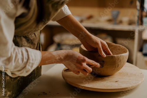 In the pottery workshop the master processes the product with a loop for clay sculpts clay dishes on the table
